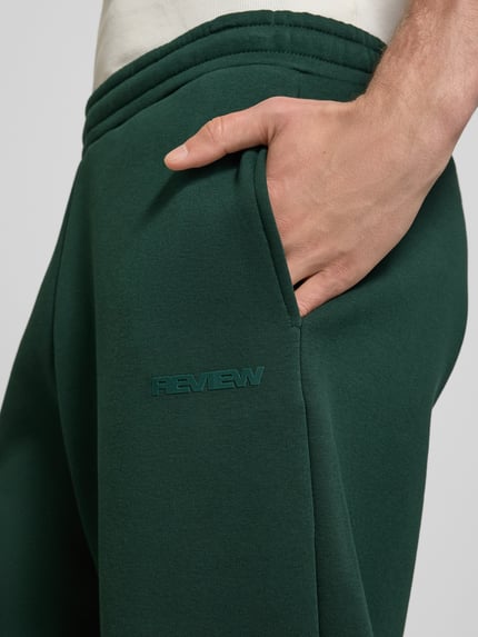 Männermodel trägt Regular Fit Sweatpants mit Gesäßtasche von REVIEW in Dunkelgrün, Baumwoll-Mix, Nahaufnahme Oberkörper. Innenbeinlänge 77 cm bei Größe M.