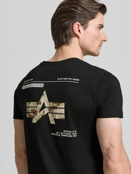 Mężczyznamodel nosi T-Shirt mit Label-Patch Modell 'Camo' od Alpha Industries z czarnej, woskowanej bawełny, prosto skrojone, nadruk i label na plecach, kontekst: T-shirt męski, żebrowany dekolt, długość tyłu w rozmiarze M: 70 cm, ujęcie: całe plecy, widok z tyłu.