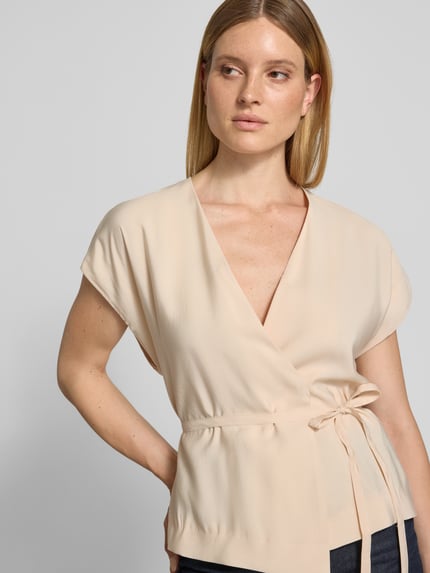 Frauenmodel trägt Weste mit V-Ausschnitt von Christian Berg Woman Selection im Modal-Mix, taillierte Passform, Wickel-Optik, abnehmbares Taillienband, Beige, glatte Textur, Nahaufnahme Oberkörper. Rückenlänge bei Größe 36: 62 cm, Schulterbreite: 45 cm, Brustweite: 49 cm.