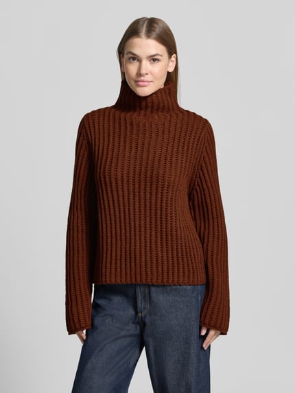 Frauenmodel trägt braunen Strickpullover mit Stehkragen Modell 'ARWIE' von DRYKORN, Material-Mix mit Alpaka-Anteil, Regular Fit, Ganzkörperansicht von vorne.