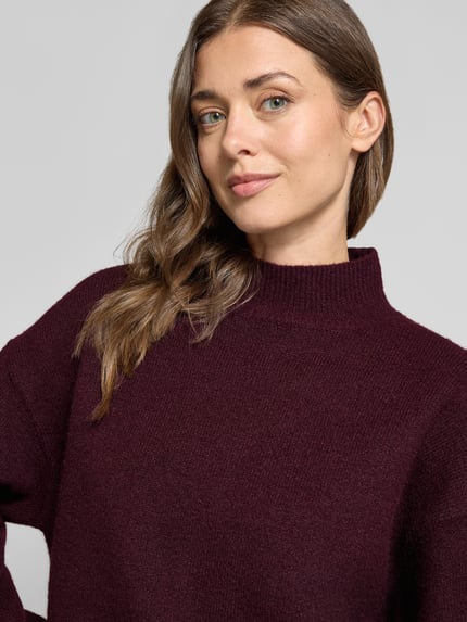Frauenmodel trägt Turtleneck-Pullover mit Woll-Anteil und Rundhalsausschnitt von Neo Noir in dunklem Bordeauxrot, Nahaufnahme Oberkörper. Modell Paulina mit gerippten Abschlüssen, Material-Mix.