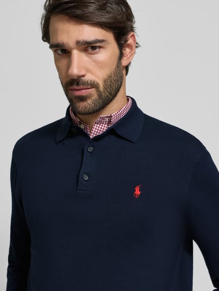 Männermodel trägt Strickpullover mit Polokragen von Polo Ralph Lauren in Dunkelblau, rote Logo-Stickerei, Nahaufnahme Oberkörper.
