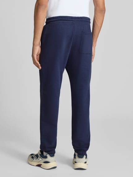 Mężczyzna nosi spodnie dresowe Straight Fit Sweatpants aus Baumwoll-Mix Model 'Kane' von JACK & JONES, mieszanka bawełny, z kieszenią z tyłu, detal z logo, elastyczny pas i zakończenia nogawek, długość wewnętrzna nogawki w rozmiarze M: 72 cm, widok całej sylwetki od tyłu.