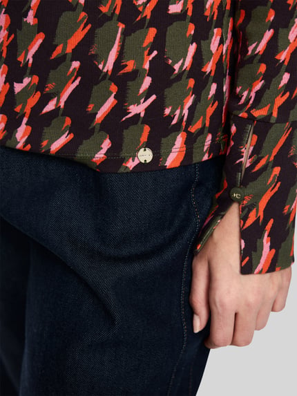 Männermodel trägt Longsleeve mit Rollkragen von Marc Cain, mieszanka bawełny i elastanu, taliowany krój, prążkowana faktura, guziki przy rękawach, długość tyłu w rozmiarze 36: 58 cm, wzór w kolory zielony, różowy i czerwony, detailaufnahme dłoni i dolnej części bluzki