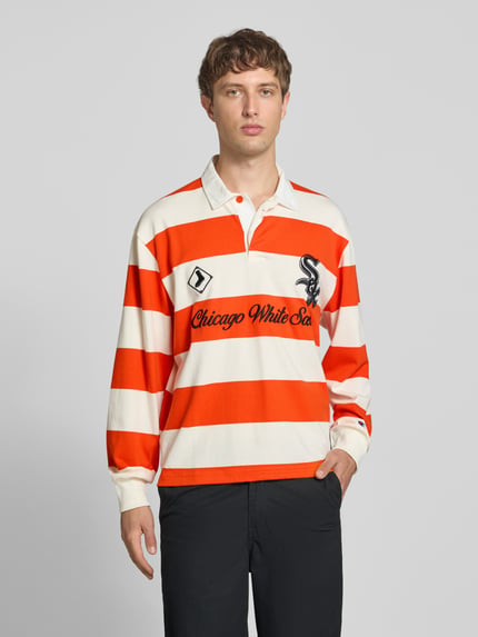 Männermodel trägt Relaxed Fit Poloshirt aus reiner Baumwolle von Champion, breite orange-weiße Blockstreifen, Statement-Stitching, Polokragen, langärmeliges Design, Ganzkörperansicht von vorne.