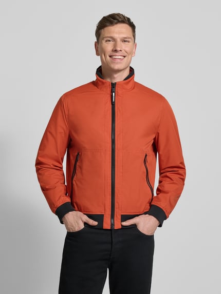Męski model nosi Regular Fit Jacke mit Stehkragen od MCNEAL, pomarańcz, wpuszczane kieszenie na zamek błyskawiczny, krój regular fit, długość tyłu w rozmiarze M 64 cm, szerokość ramion w rozmiarze M 43 cm, szerokość klatki piersiowej w rozmiarze M 55 cm, długość rękawów w rozmiarze M 67 cm, całkowity widok z przodu