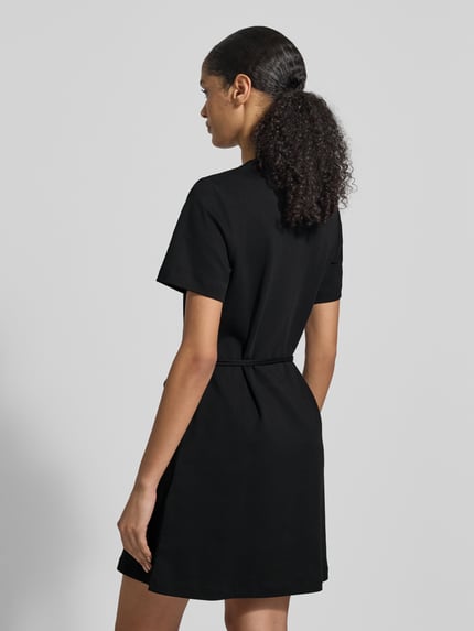Frauenmodel trägt Tailliertes Sweatkleid aus reiner Baumwolle von Tommy Hilfiger in Optik: Unifarben, Passform: Tailliert, Mini-Länge, Logo-Stitching, Rundhals, Kurzarm, gerader Saum, Materialverarbeitung: Interlock, Ganzkörperansicht Rückansicht.