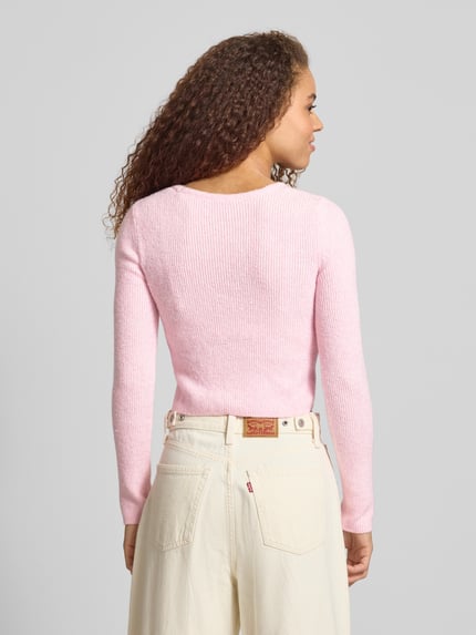 Frauenmodel trägt Regular Fit Strickjacke mit Perl-Optik-Knöpfen Modell 'RICA LIFE' von ONLY in zartem Rosa, Optik: Unifarben, Rippstrick, Passform: Regular-Fit, Verschluss: einreihige Knopfleiste, Ausschnitt: V-Ausschnitt, Ärmelform: Langarm, Materialverarbeitung: Rippstrick, Ganzkörperansicht Rückansicht.