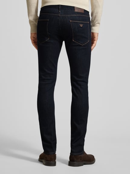 Männermodel trägt Slim Fit Jeans mit Logo-Applikation von Emporio Armani in dunklem Blau, 5-Pocket-Design, Ganzkörperansicht Rückansicht.