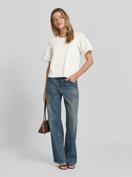 Frauenmodel trägt Regular Fit T-Shirt mit Smok-Detail von Comma aus reiner Baumwolle, ausgestellte Ärmel, kurzärmelig, Rundhalsausschnitt, Rückenlänge bei Größe 36: 54 cm, in Cremefarbe, kombiniert mit Jeans, Ganzkörperansicht von vorne.