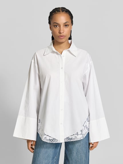 Kobiece model prezentuje Oversized Hemdbluse mit Spitzenbesatz od Officine Générale z bawełny, krój oversized, kołnierzyk koszulowy, długi rękaw, obszycie koronką na dole, długość tyłu w rozmiarze 36: 74 cm, długość rękawów w rozmiarze 36: 57 cm, widok całej sylwetki z przodu.
