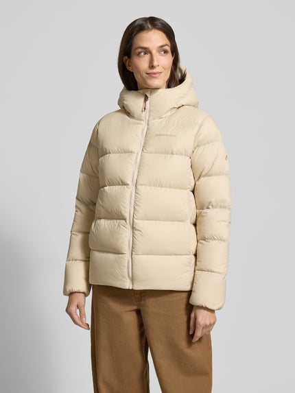 Frauenmodel trägt cremefarbene Steppjacke mit Label-Stitching Modell 'FROST DOWN' von PEAK PERFORMANCE, Regular-Fit, Kapuze, Reißverschluss, Ganzkörperansicht von vorne. Rückenlänge 64 cm, Schulterbreite 41 cm, Brustweite 56 cm, Ärmellänge 64 cm bei Größe S.