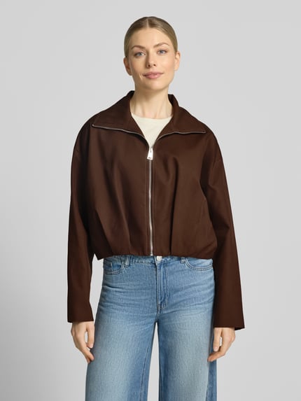 Frauenmodel trägt Blouson mit Umlegekragen Modell 'DANTES' von MANGO aus reiner Baumwolle in Braun, Reißverschluss, Ganzkörperansicht von vorne.