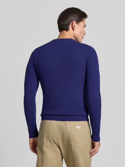 Männermodel trägt Slim Fit Strickpullover aus reiner Wolle mit Label-Stitching von MCNEAL in Blau, Ganzkörperansicht Rückansicht. Rückenlänge 66 cm, Ärmellänge 69 cm, gerippte Abschlüsse, Herren Strickpullover, feine Textur.