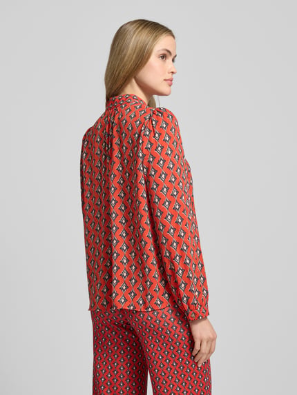 Frauenmodel trägt Regular Fit Bluse im Allover-Look mit Volants von Marc Cain in Rot mit grafischem Muster, Stehkragen, Rückansicht, Ganzkörperansicht. Rückenlänge bei Größe 36: 60 cm, Ärmellänge: 59 cm.