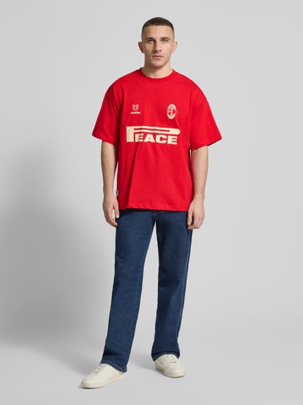 Męski model nosi Regular Fit T-Shirt mit Logo-Print von ANOTHER COTTON LAB, czysta bawełna, krój regular fit, okrągły dekolt, długość tyłu w rozmiarze M: 71 cm, przód w pełnej sylwetce.