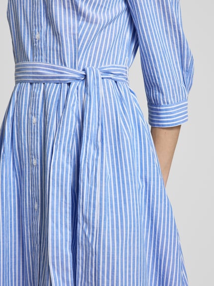Männermodel trägt Hemdblusenkleid mit Bindegürtel und 3/4-Arm von Oui, bawełna, linia a, sukienka midi, kołnierzyk koszulowy, listwa guzikowa, wiązany pasek, rękaw o dł. 3/4, długość tyłu w rozmiarze 36: 120 cm, szerokość w rozmiarze 36: 48 cm, długość rękawów: 46 cm, niebieskie i białe paski, gładka tekstura, detailaufnahme.