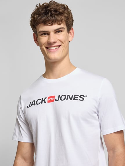 Męski model nosi T-Shirt z label-printem model 'CORP' od JACK & JONES, biały, bawełna z domieszką wiskozy, prosty krój, ujęcie od przodu.