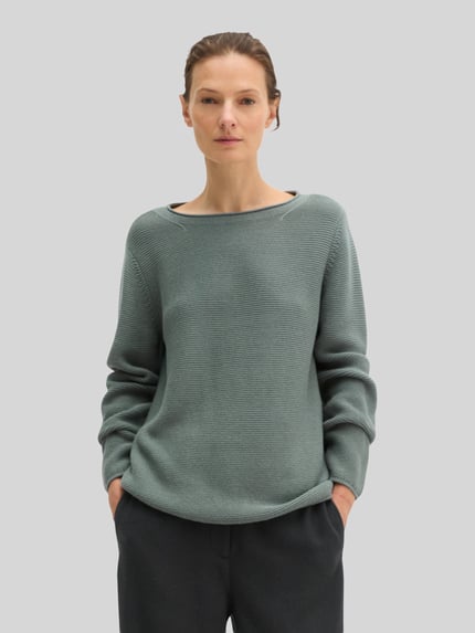 Frauenmodel trägt Regular Fit Pullover aus reiner Baumwolle von MARC O’POLO in unifarbener, gerippter Strickoptik, Nahaufnahme Oberkörper.