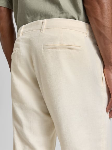 Männermodel trägt Relaxed Fit Bundfaltenhose aus Baumwoll-Mix mit Leinen-Anteil Modell 'LOUIS-W' von Strellson in Beige, Nahaufnahme Rückansicht. Material wirkt meliert, strukturierte Twill-Oberfläche mit Gürtelschlaufen und Label Patch.