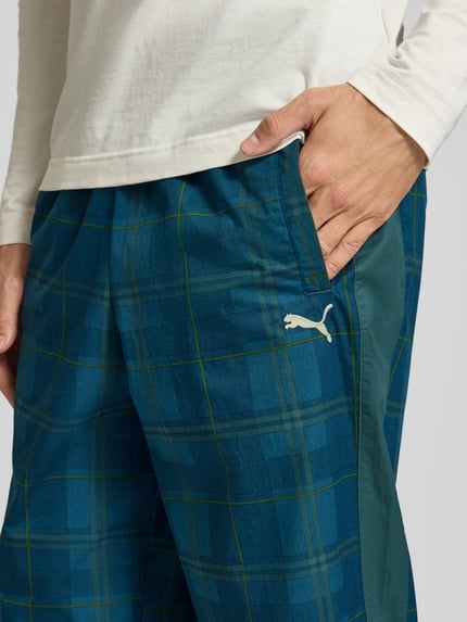 Männermodel trägt Relaxed Fit Trackpants aus reiner Baumwolle von PUMA mit Tartan Allover-Muster und Logo-Stitching, Nahaufnahme Oberkörper.