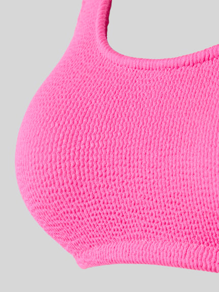 Vrouwenmodel draagt Bikini-Oberteil met Label-Detail Modell 'JUSTIN' van Banana Moon, felroze structuurstof, detailopname, materiaal-mix met stretch.
