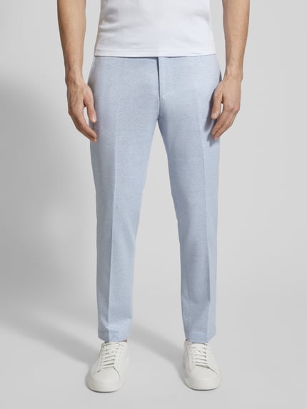 Männermodel trägt hellblaue Hose mit Bügelfalte, kombiniert mit weißem Shirt und Sneakers, glatte Textur, Nahaufnahme Beine.