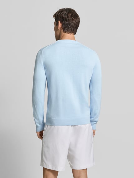 Männermodel trägt hellblauen Regular Fit Pullover aus Baumwoll-Mix von Lacoste, weiße Shorts, Ganzkörperansicht Rückansicht. Herren Pullover von Lacoste