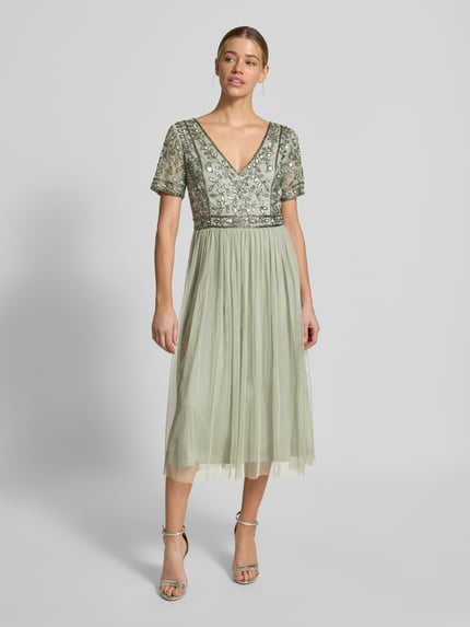 Modelka kobieca nosi Knielanges Kleid mit floralem Pailettenbesatz od LACE & BEADS, florystyczny pailettenbesatz, krój slim fit, dekolt V, siateczka, krótkie rękawy, długość tyłu w rozmiarze S: 100 cm, szerokość w rozmiarze S: 42 cm, długość rękawa w rozmiarze S: 19 cm, jasna zieleń, detale w kwiaty, zwiewna tekstura, widok całej sylwetki od przodu.