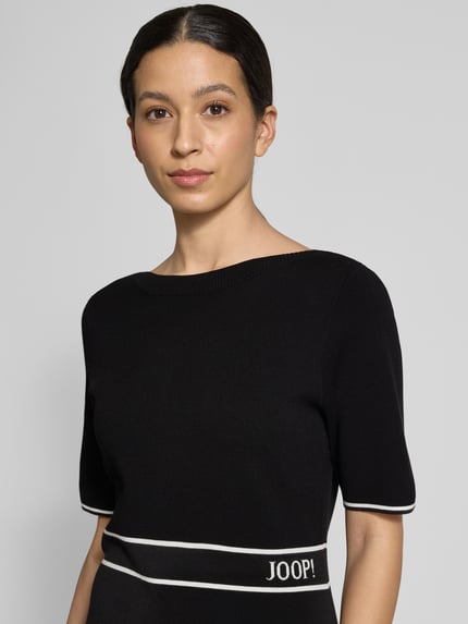 Frauenmodel trägt Regular Fit Kleid aus Viskose-Mix Modell 'Kirla' von JOOP! in Schwarz mit Strick-Optik, Halbarm, Logo-Stitching, Nahaufnahme Oberkörper.