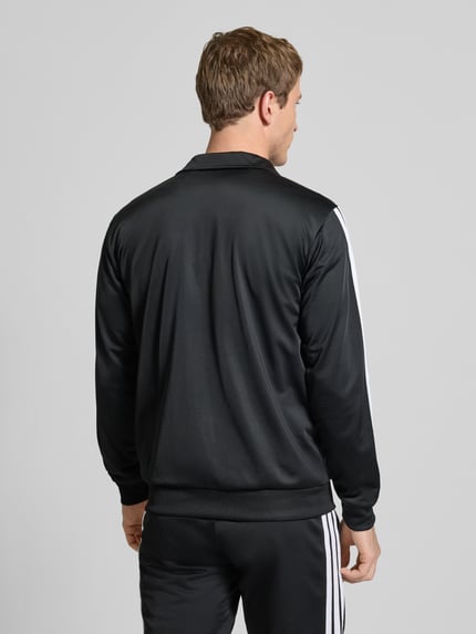 Männermodel trägt Trainingsanzug mit Stretch-Anteil von adidas Sportswear, Schwarz mit weißen Streifen, Elastischer-Material-Mix, Gerade Passform, Stehkragen, Durchgehender Reißverschluss, Elastische Abschlüsse, Elastischer Bund, Eingrifftaschen, Label-Details, Ganzkörperansicht Rückansicht