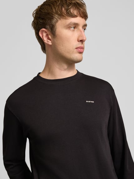 Männermodel trägt Langarmshirt mit Logo-Schriftzug von G-Star RAW in Schwarz, strukturierte Jersey-Optik, Nahaufnahme Oberkörper.