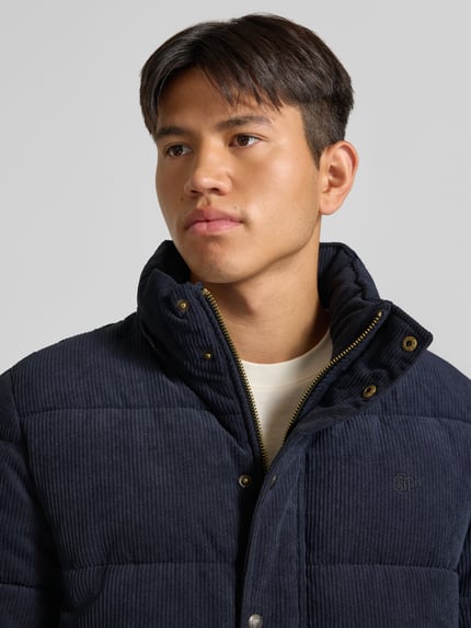 Männermodel trägt Steppjacke in Cord-Optik von Superdry, granatowy, imitacja sztruksu, Kaptur, listwa guzikowa, Nahaufnahme Oberkörper, krój prosty, długość tyłu w rozmiarze M 72 cm, szerokość ramion w rozmiarze M 48 cm, szerokość klatki piersiowej w rozmiarze M 60 cm, długość rękawów w rozmiarze M 70 cm