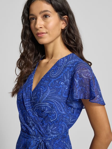 Frauenmodel trägt knielanges Kleid mit V-Ausschnitt Modell 'WANDELLA' von Lauren Ralph Lauren in Wickel-Optik, blau gemustert, Nahaufnahme Oberkörper.