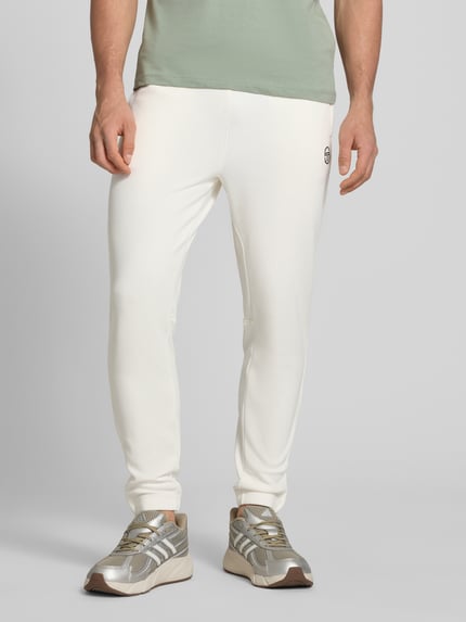 Męski model nosi Slim Fit Tracksuit mit Logo-Stitching model 'Egeo' von SERGIO TACCHINI, mieszanka bawełny, krój slim fit, stójka, wyhaftowane logo, zamek błyskawiczny, elastyczne wykończenia, jasny kolor, gładka faktura, zdjęcie z przodu, detailaufnahme dolna część ciała.