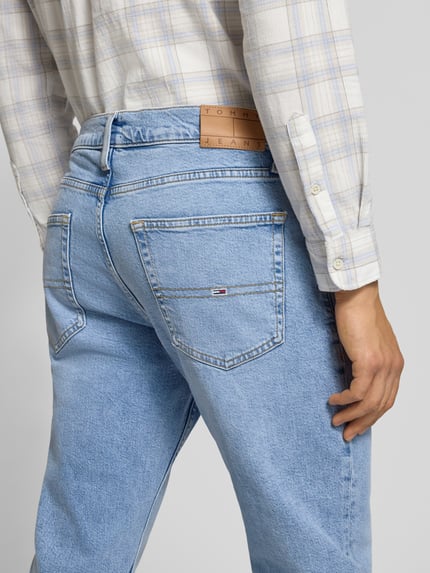 Mannenmodel draagt Straight Fit Jeans uit katoenmix van Tommy Jeans met melangelook, labelpatch en 5-pocketmodel, detailopname rug.