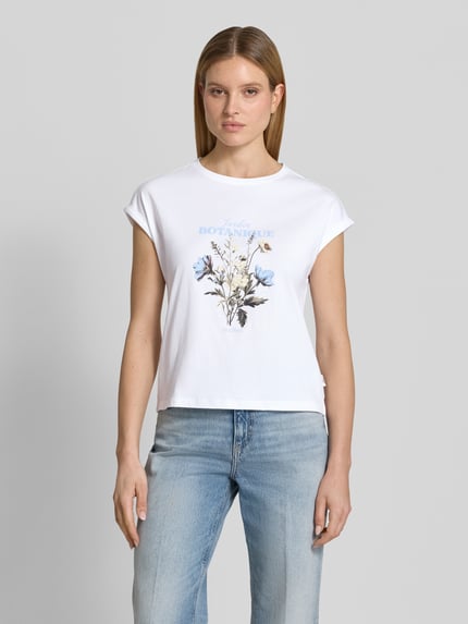 Kobiece modelka nosi Relaxed Fit T-Shirt aus reiner Baumwolle od s.Oliver RED LABEL, biały kolor, kwiatowy front-print, okrągły dekolt, krótkie rękawy z wywinięciem, tekstura gładka, fason relaxed fit, widok całej sylwetki z przodu.