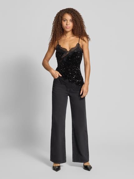 Frauenmodel trägt Regular Fit Blusentop mit Paillettenbesatz Modell 'PCKAMMY' von PIECES in Schwarz mit Spitze und asymmetrischem Saum, Ganzkörperansicht von vorne.