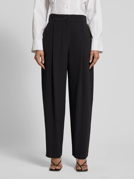 Frauenmodel trägt czarne Relaxed Fit Hose mit Bundfalten von ARMANI EXCHANGE, szerokość w rozmiarze 36: 38 cm, długość nogawki wewnętrznej w rozmiarze 36: 76 cm, kieszenie z przodu, zapięcie na guzik i zamek, całkowity widok z przodu