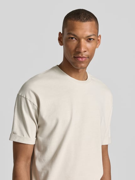 Männermodel trägt T-Shirt mit Ärmelaufschlag und Rundhalsausschnitt von Drykorn aus Reine Baumwolle Regular-Fit in Beige, Nahaufnahme Oberkörper.
