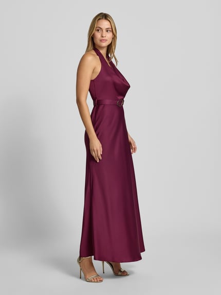 Frauenmodel trägt Abendkleid mit Neckholder von Rinascimento in dunklem Violett, taillierte Passform, Stoffgürtel, Maxikleid, Ganzkörperansicht von vorne.