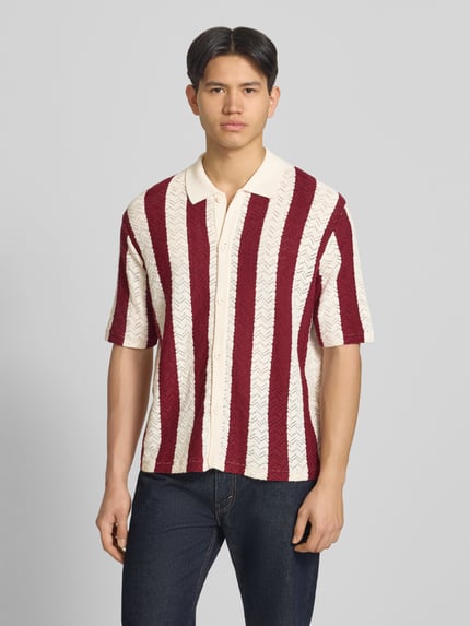 Männermodel trägt Regular Fit Poloshirt mit Knopfleiste Modell 'TYLER' von Jack & Jones aus Baumwoll-Mix mit roten und weißen Streifen, 1/2-Arm, Ganzkörperansicht von vorne.