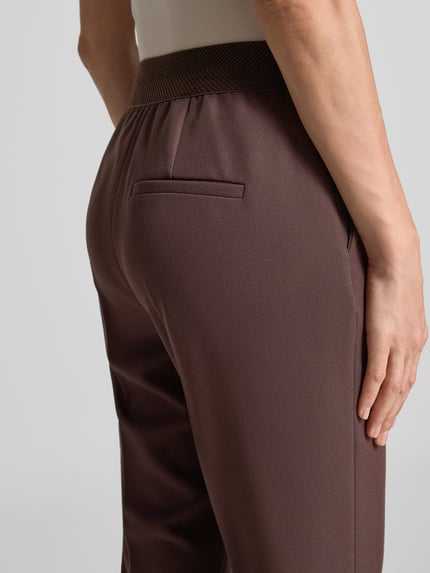 Frauenmodel trägt Regular Fit Anzughose mit elastischem Bund von s.Oliver BLACK LABEL in Dunkelbraun, Struktur sichtbar, Nahaufnahme Rückansicht.