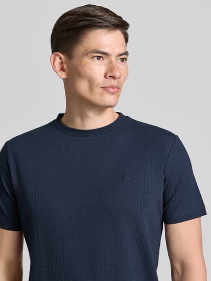 Mannenmodel draagt T-shirt met structuurpatroon en gestikt logo van Lerros in donkerblauw katoenmix met stretch, regular fit, ronde hals, ruglengte maat M 75 cm, Nahaufnahme Oberkörper.