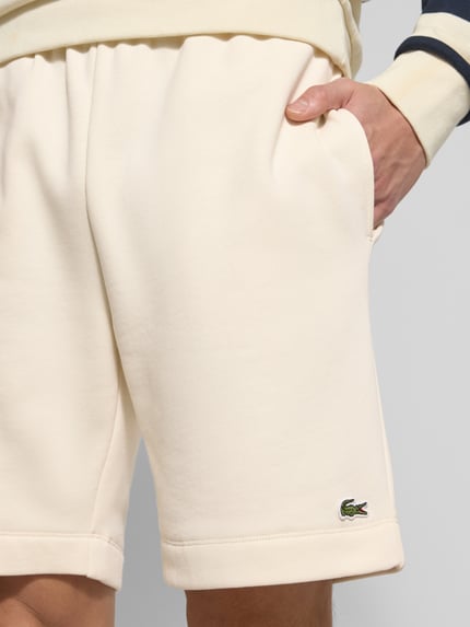 Mężczyznamodel nosi Regular Fit Sweatshorts aus Baumwoll-Mix od Lacoste w jednolitym kolorze, z elastycznym pasem i bocznymi kieszeniami, materiał sweat z bawełnianej mieszanki, naszywka z logo, zbliżenie na przednią część szortów, ujęcie detailaufnahme.