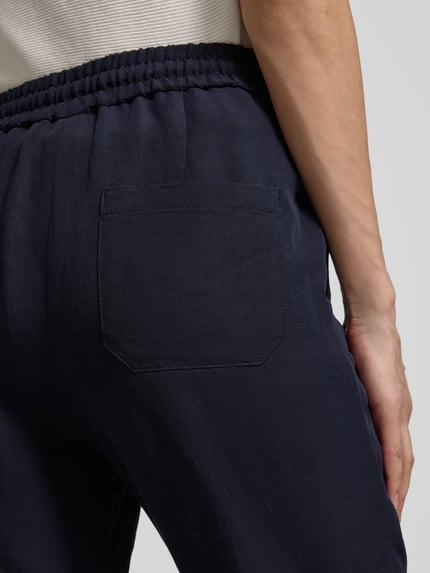 Männermodel trägt Straight Fit Stoffhose aus Viskose-Mix mit Leinen-Anteil von Marc Cain, materiał stylizowany na len, wpuszczane kieszenie, tunel w pasie, szerokość w rozmiarze 36: 37 cm, długość wewnętrzna nogawki w rozmiarze 36: 66 cm, ciemny niebieski, tekstura gładka, detailaufnahme tylnej części