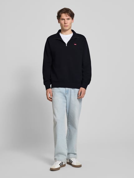 Męskimodel nosi Regular Fit Sweatshirt aus reiner Baumwolle von Levi's®, bluza czarna, jasnoniebieskie spodnie, Ganzkörperansicht von vorne.