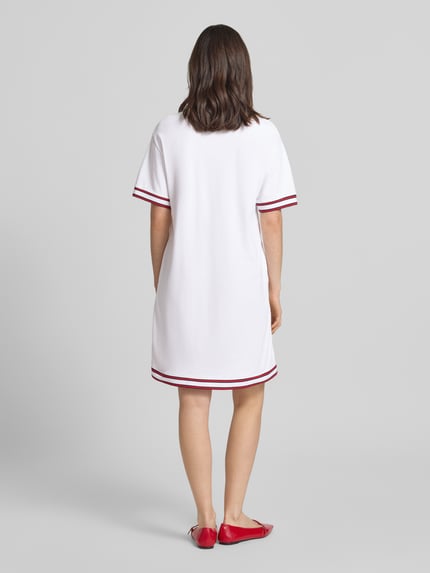 Vrouwenmodel draagt knielange Polojurk met label-stitching model 'Tasa' van JOOP!, wit met rode contraststrepen, katoenen elasthaansamenstelling, rechte fit, rugaanzicht volledige lengte.
