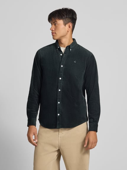 Männermodel trägt Regular Fit Freizeithemd mit Logo-Stitching Modell 'MADISON' von Carhartt Work In Progress, Nahaufnahme Oberkörper. Reine Baumwolle, dunkelgrüne Farbe, sichtbare Knopfleiste und Button-Down-Kragen, dezente Struktur.