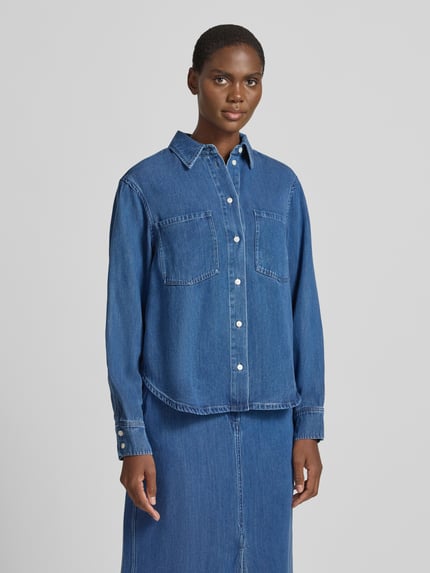 Frauenmodel trägt Jeansbluse mit Brusttaschen Modell 'SABEXY' von Samsøe Samsøe in klassischem Blau, strukturierte Optik, gerader Schnitt, Knopfleiste, Kentkragen und Sportmanschetten, Lyocell-Material, abgerundeter Saum, Ganzkörperansicht von vorne.